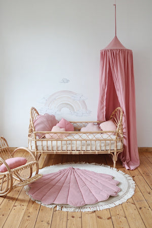 Powder pink shell playmat beneath a rattan child’s bed and matching pink canopy