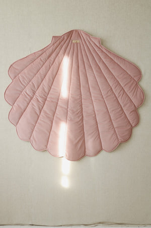 Powder pink shell-shaped textile playmat hanging vertically as children’s room wall décor