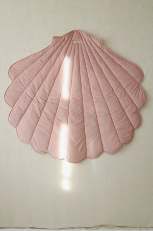 Powder pink shell-shaped textile playmat hanging vertically as children’s room wall décor