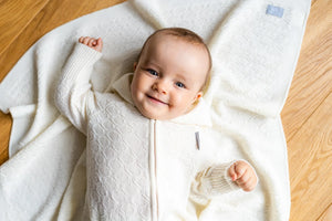 Bébé souriant en grenouillère tricotée crème sur une couverture assortie à motif losanges
