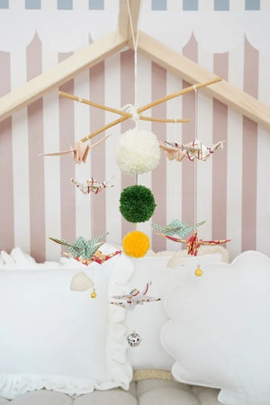 Moi Mili Vintage Vibe origami mobile with patterned paper cranes and colourful pompoms above white nursery cushions