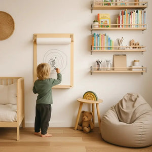 Child drawing on wall-mounted paper roll in nursery with wooden shelves, crib, and rainbow stool