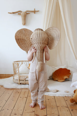 Close-up of a child holding a woven elephant mask beside a cream cotton canopy