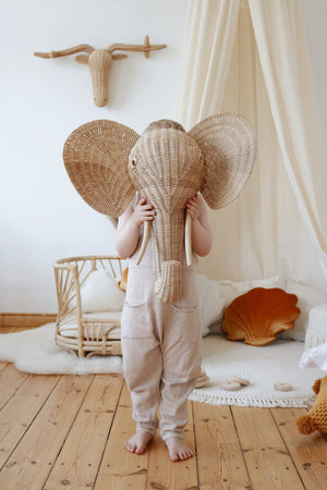 Close-up of a child holding a woven elephant mask beside a cream cotton canopy