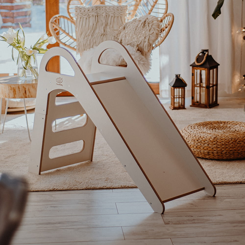 Scivolo indoor minimalista in legno bianco per bimbi, in una stanza calda e accogliente con decorazioni boho, sedia in vimini e lanterne su un tappeto soffice.