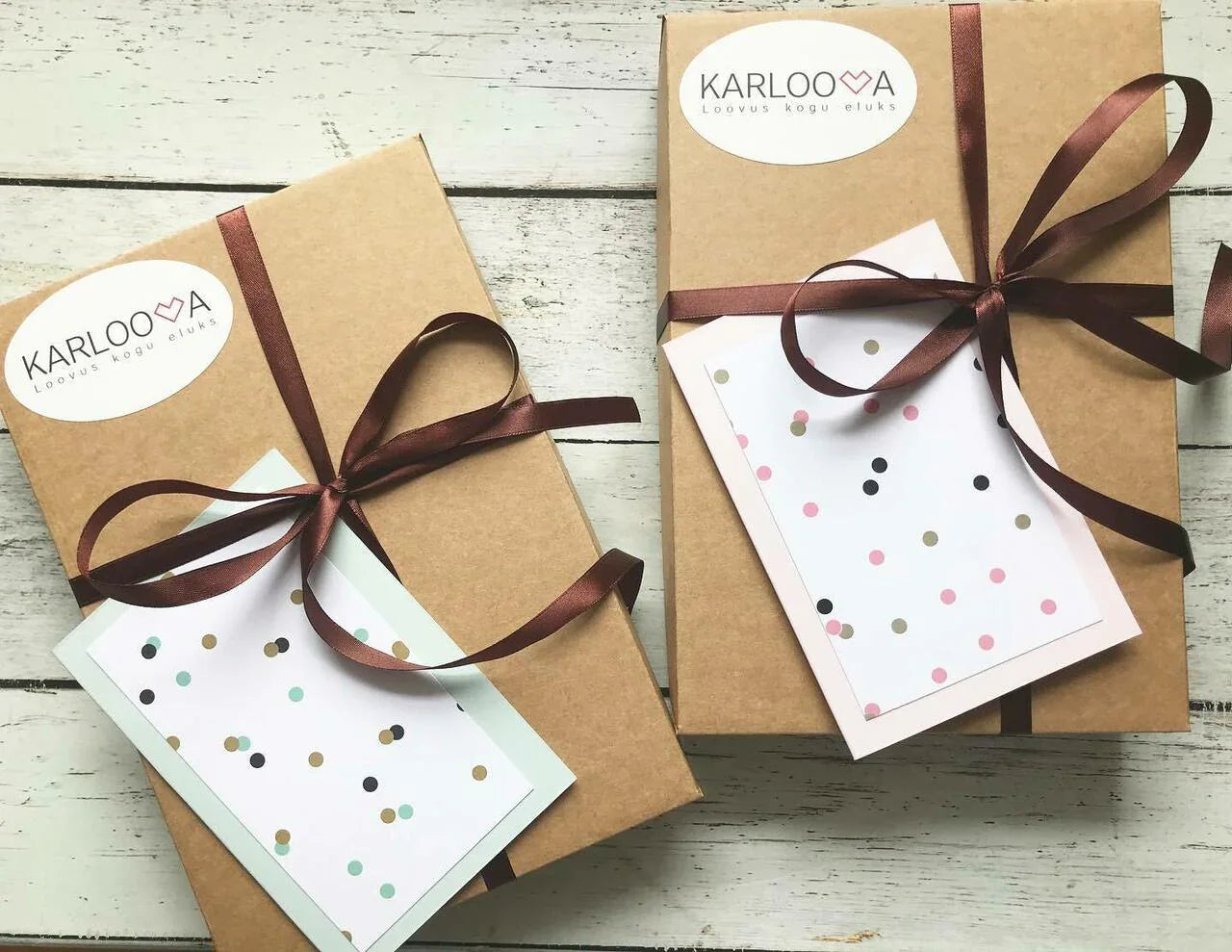 Two kraft gift boxes with brown ribbons and polka dot greeting cards on rustic wood