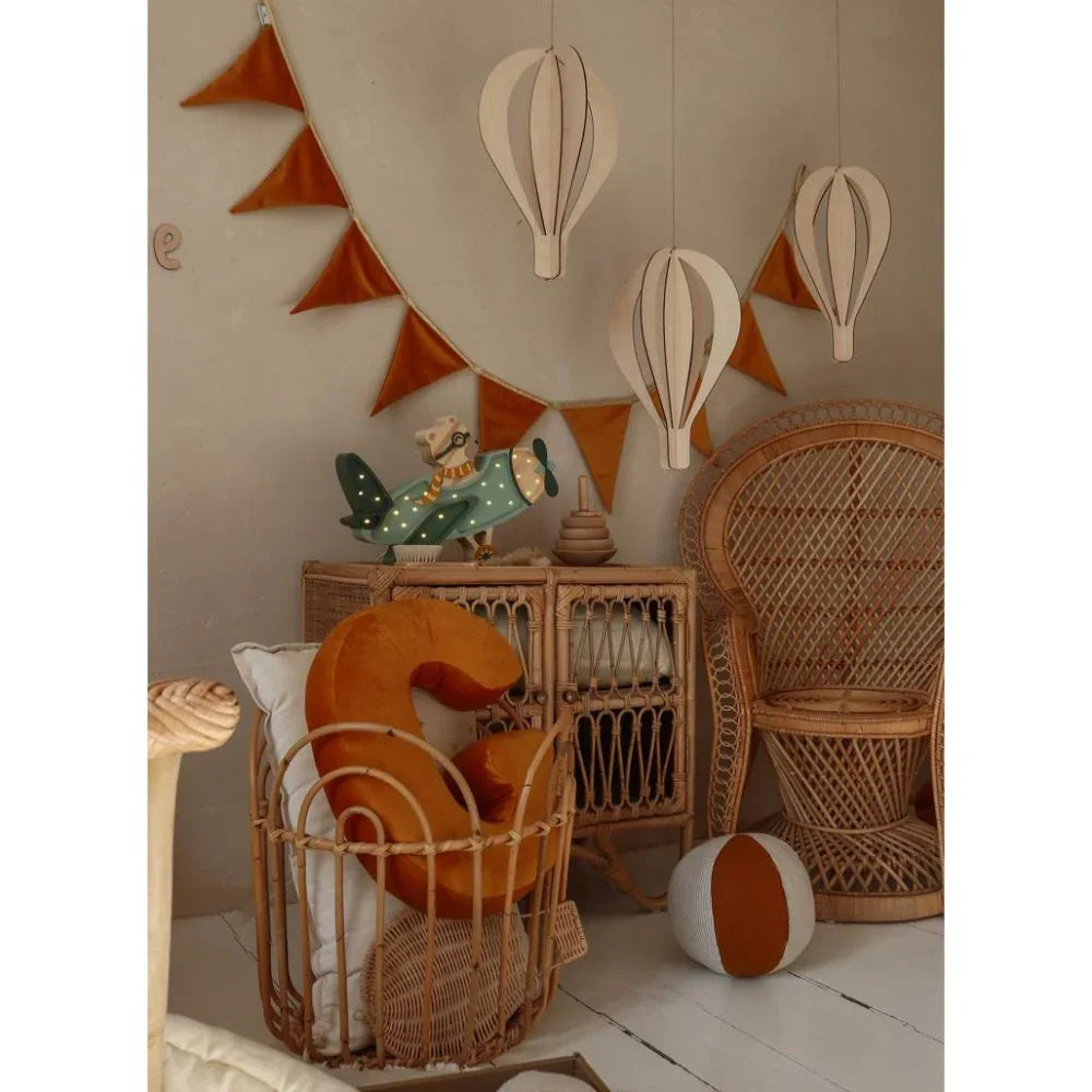 Rattan nursery furniture with orange velvet number pillow, hanging paper hot air balloons, and vintage airplane decor