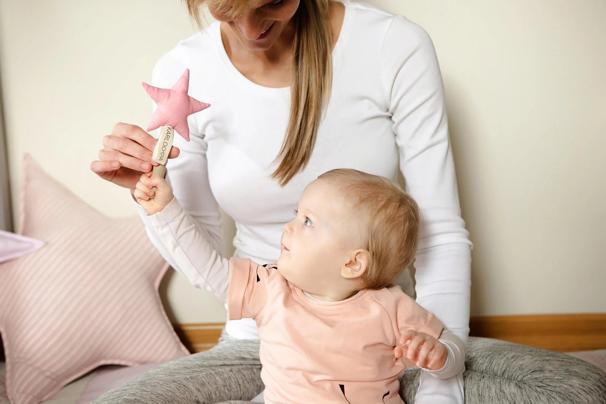 Bebé alcanzando un juguete de peluche de estrella rosa con un adulto, fondo de decoración pastel.