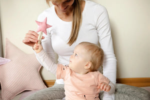 Bebé alcanzando un juguete de peluche de estrella rosa con un adulto, fondo de decoración pastel.