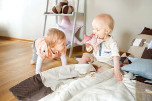 Dos bebés jugando en una habitación infantil con almohadas en forma de estrella pastel y alfombras de juego de algodón suave.