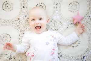 Bebé sonriente sobre una manta de ganchillo color crema con juguete de peluche de estrella rosa.