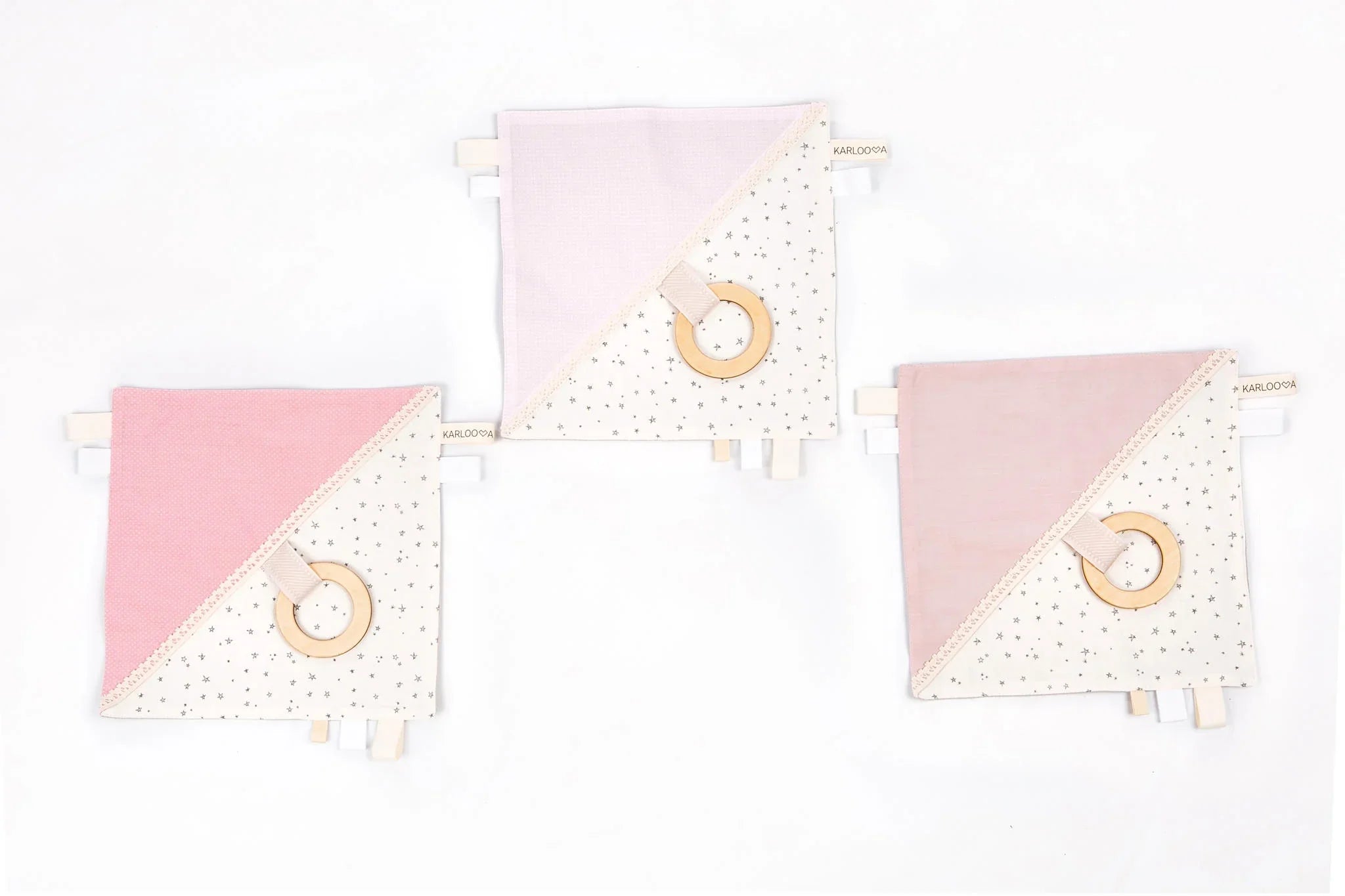 Set de tres doudous para bebé en rosa pastel y crema con patrones de estrellas y aros de dentición de madera.