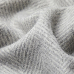 Gros plan sur la texture douce d'un jeté en laine d'alpaga gris clair et blanc à motif chevrons