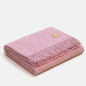 Couverture jetée en laine d'alpaga rose à motif chevrons, pliée avec soin, finitions à franges classiques et petit écusson en cuir ALPAKA sur fond clair.