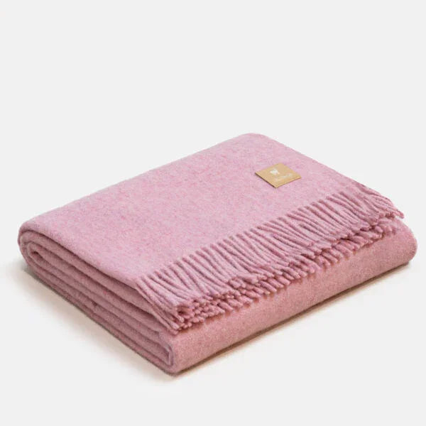 Couverture jetée en laine d'alpaga rose à motif chevrons, pliée avec soin, finitions à franges classiques et petit écusson en cuir ALPAKA sur fond clair.