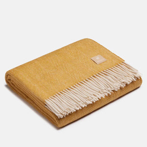 Gros plan sur la texture douce d'un jeté en laine d'alpaga jaune moutarde et blanc à motif chevrons