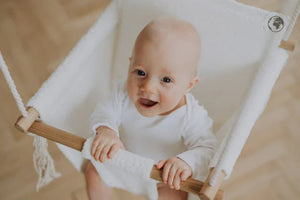 Baby in white cotton hammock swing with wooden frame, nursery decor