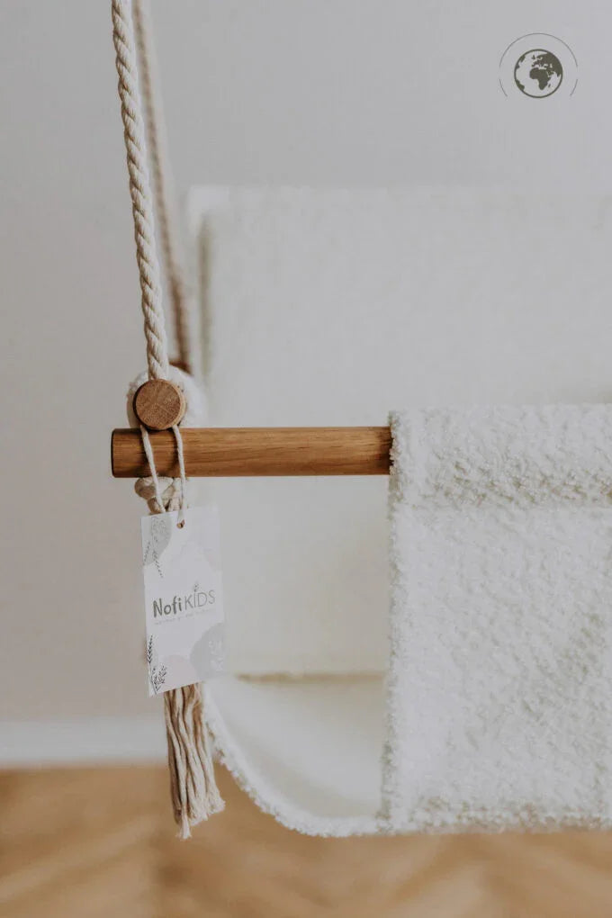 White fluffy baby hammock with wooden bar and rope, Noft Kids tag visible, nursery decor