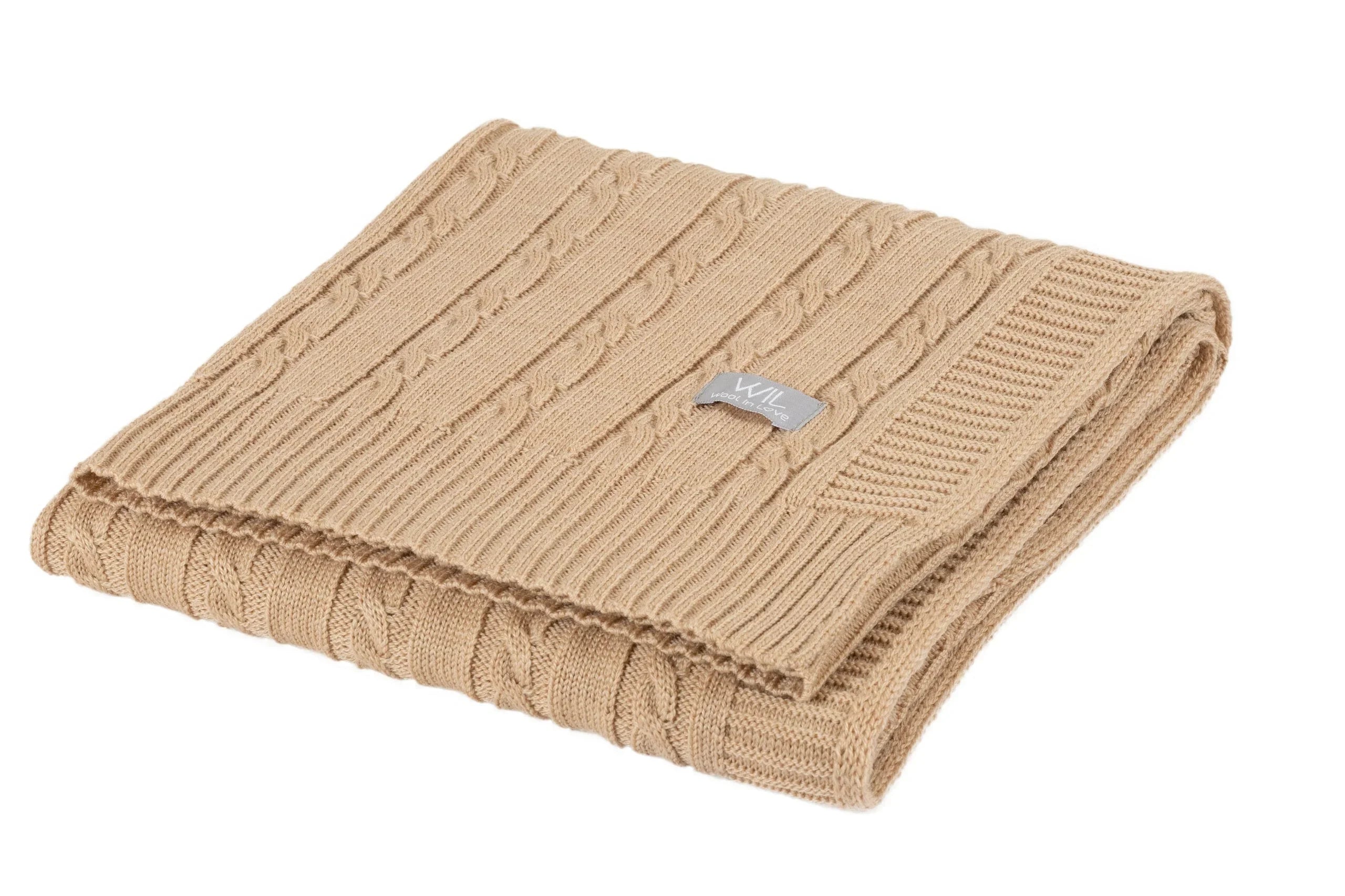 Couverture bébé en tricot torsadé beige pliée avec bords côtelés et étiquette tissée