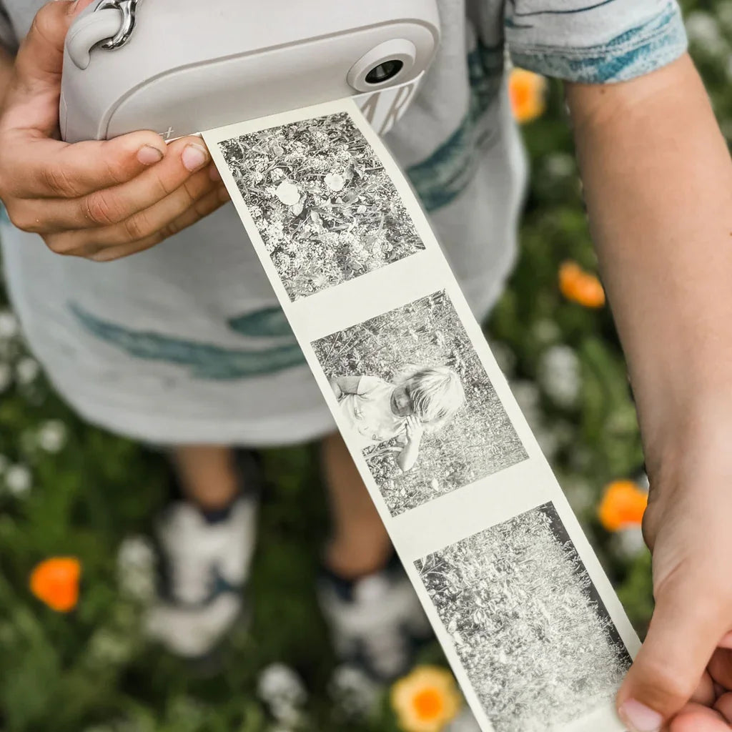 Child holding instant camera with black and white photo strip in garden