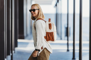 Donna sorridente che cammina in città indossando l'elegante zaino fasciatoio in similpelle Ally Scandic color cappuccino.