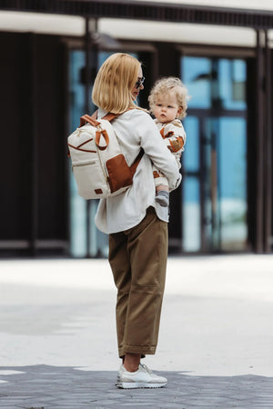 Mamma che tiene in braccio il suo bambino indossando lo zaino fasciatoio in similpelle Ally Scandic (bianco e cappuccino).
