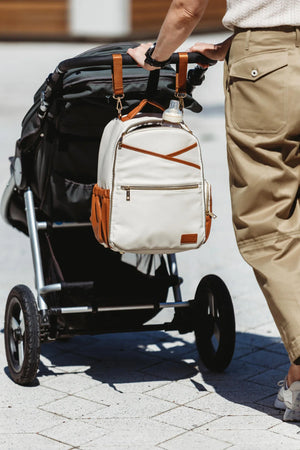 Genitore che spinge un passeggino all'aperto con lo zaino fasciatoio Ally Scandic color cappuccino appeso in sicurezza al manubrio.