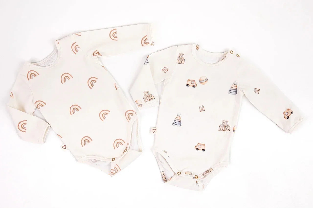 Set of two cream baby bodysuits with rainbow and toy patterns, long sleeves, cotton fabric