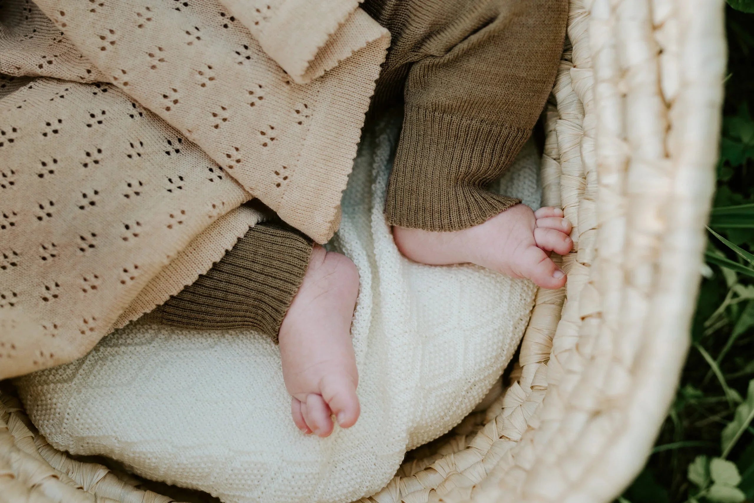 Pieds de bébé en tricot marron sur couverture tissée crème dans un panier naturel