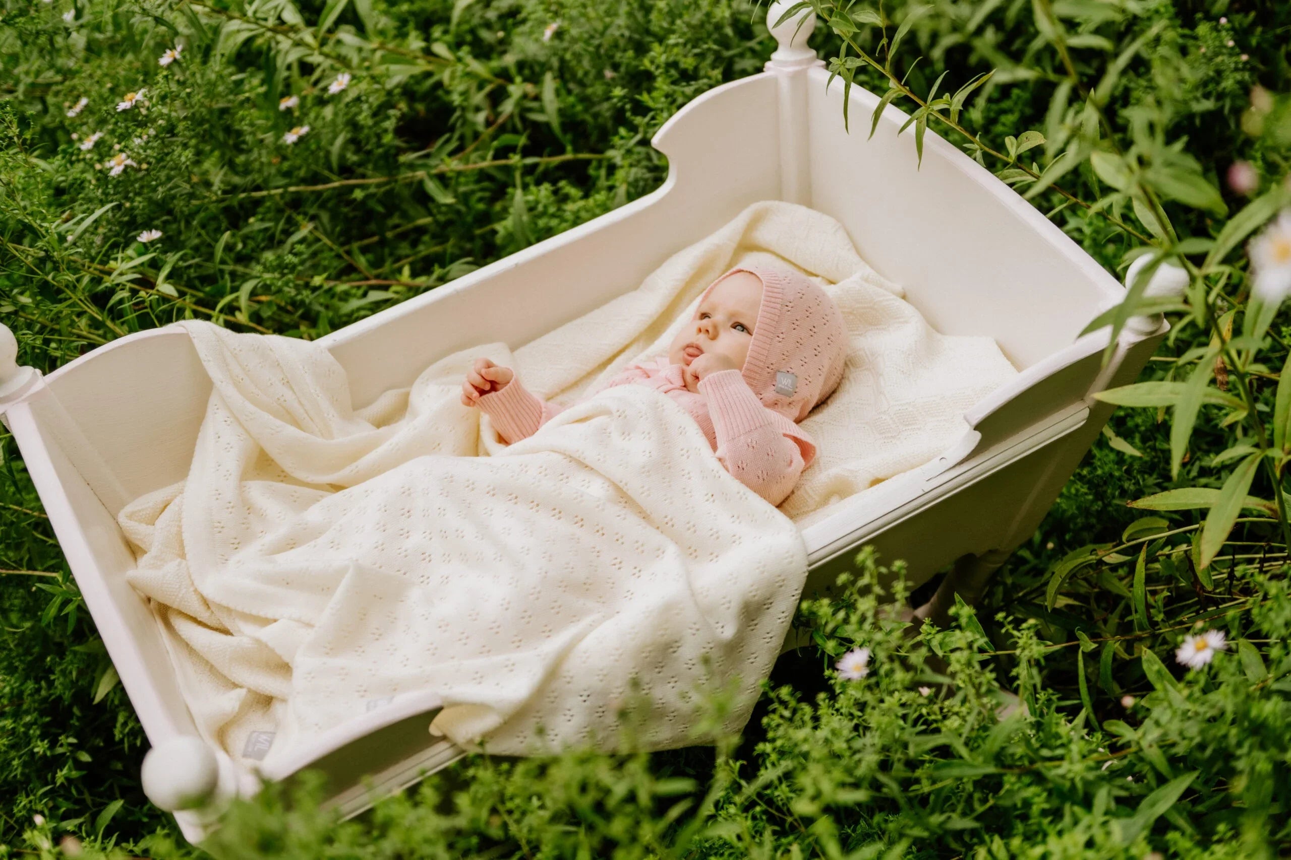 Bébé fille avec tricot rose et couverture crème en tricot dans un berceau blanc en extérieur