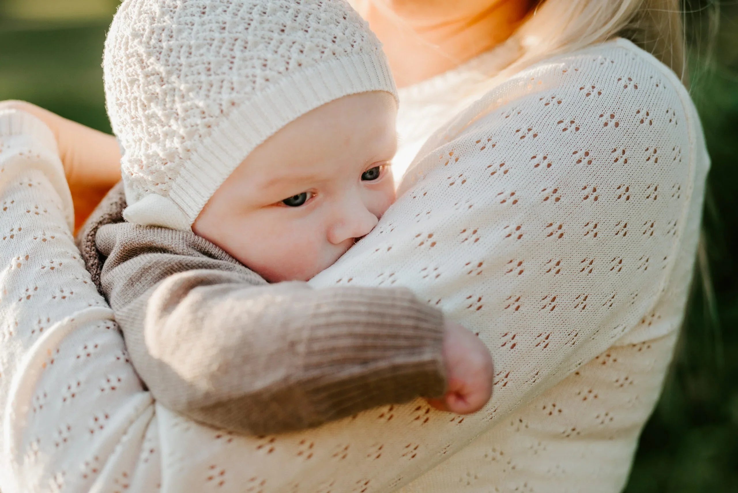 Bébé dans les bras portant un bonnet et un gilet en tricot crème, vêtements bébé naturels