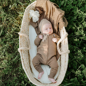 Bébé dans un couffin en osier portant des tricots marron et un bonnet sur fond d'herbe