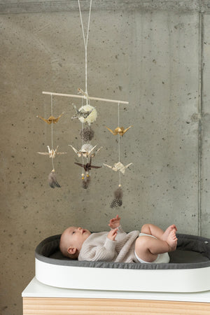 Baby observing the Gold Dust origami mobile above a changing mat