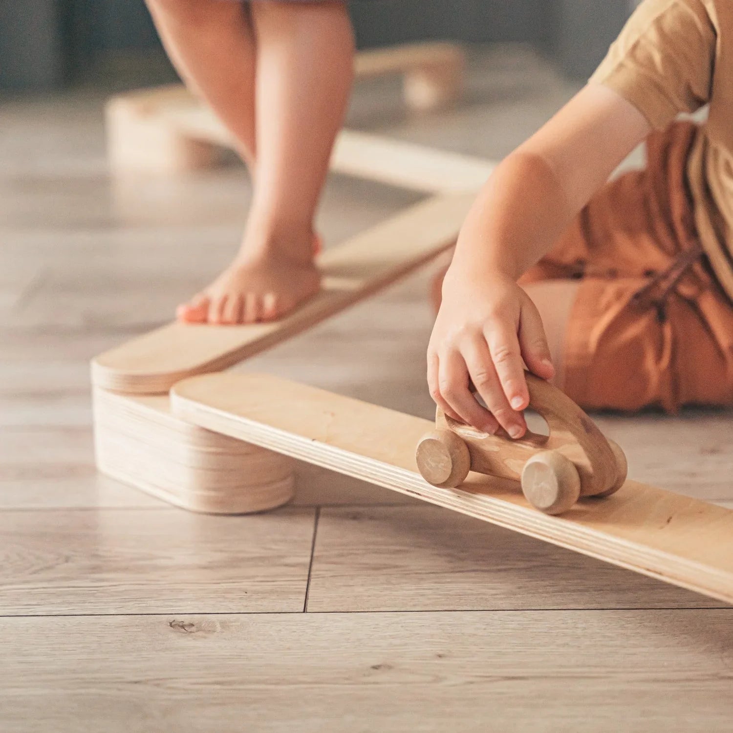 Set de cuatro vigas de equilibrio de madera con un niño caminando y coche de juguete de madera sobre un suelo de madera clara