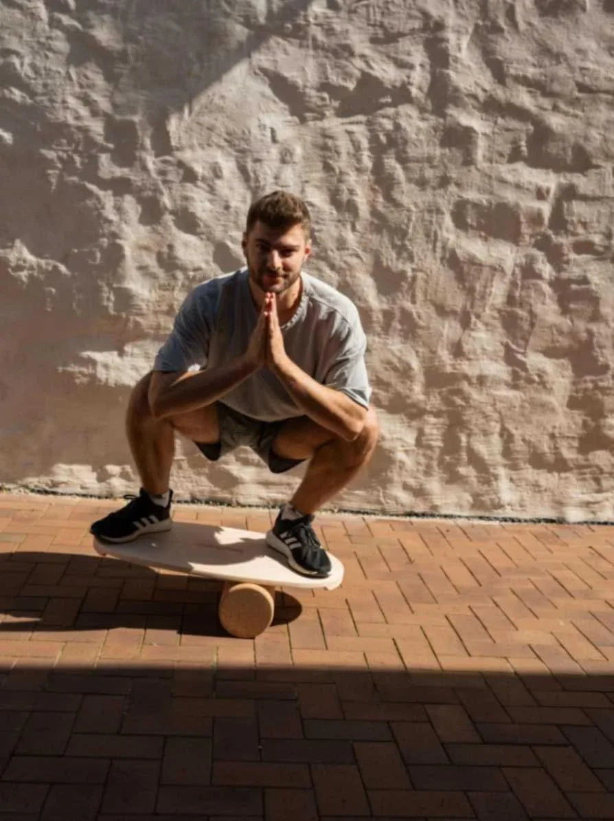 Man balancing in squat on wooden balance board with cork roller on outdoor brick patio