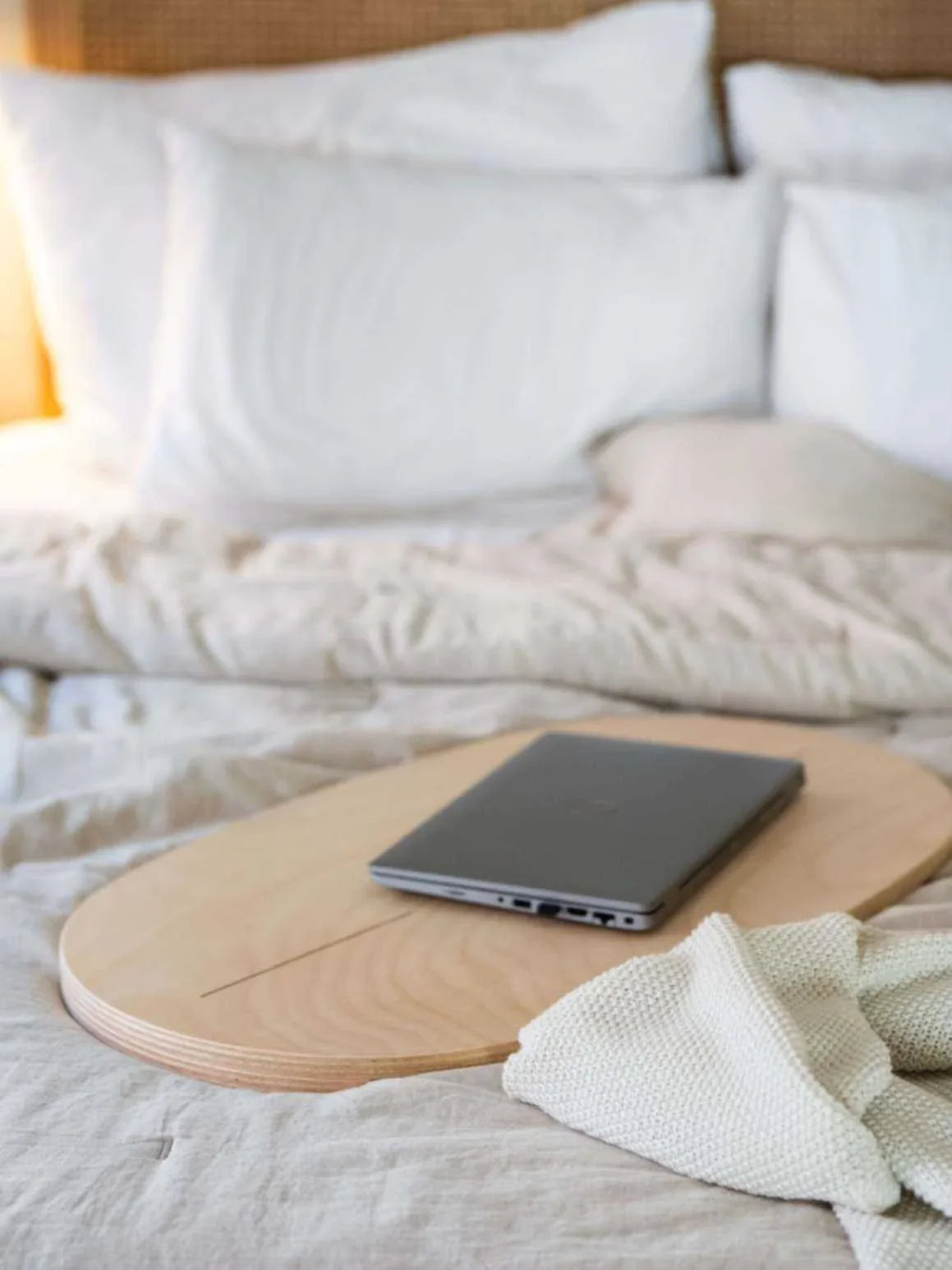 Tabla de equilibrio de madera y rodillo de ejercicio gris sobre ropa de cama neutra, portátil colocado encima