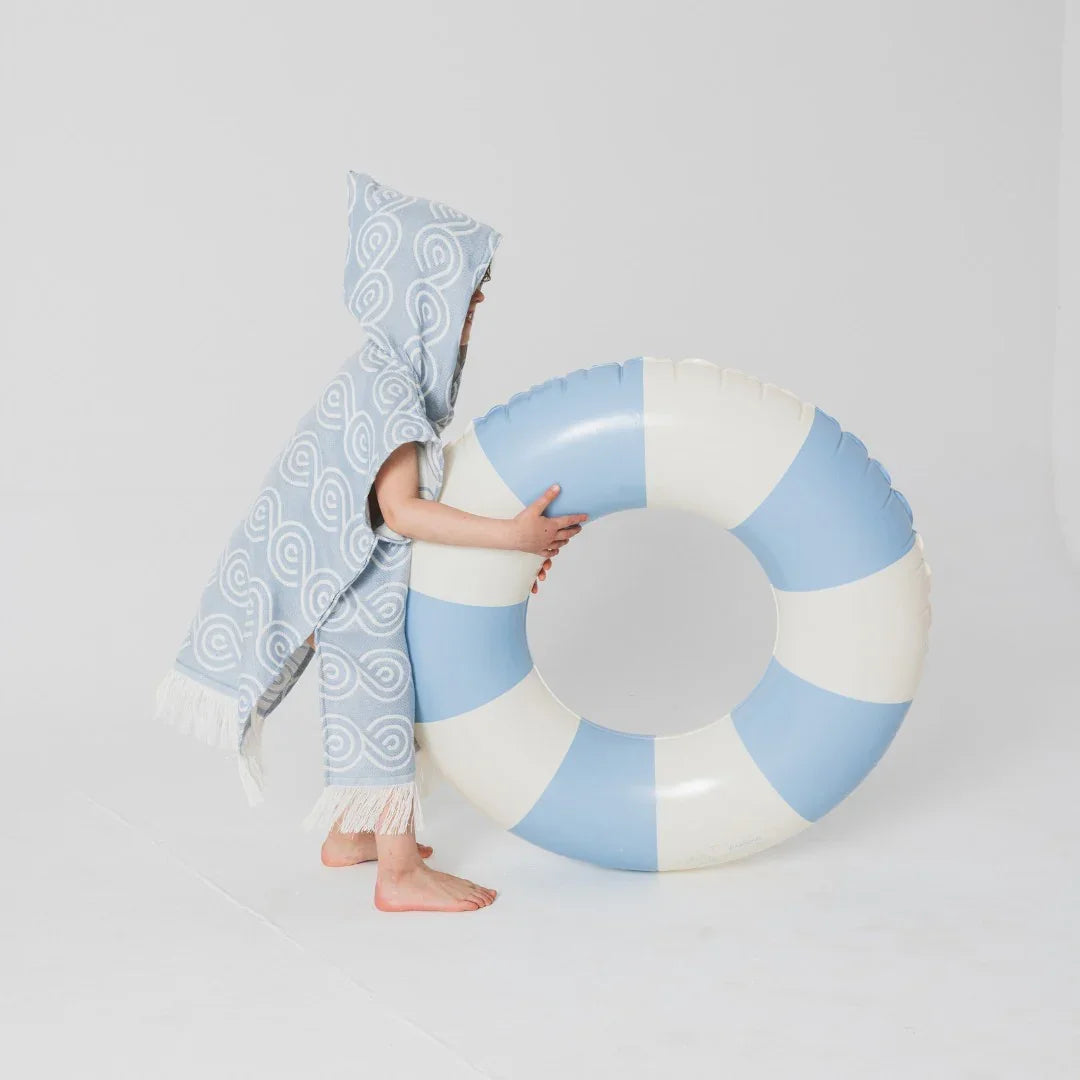Kind trägt blauen Bambus-Badeponcho mit Kapuze und weißem Muster, daneben ein Pool-Schwimmtier