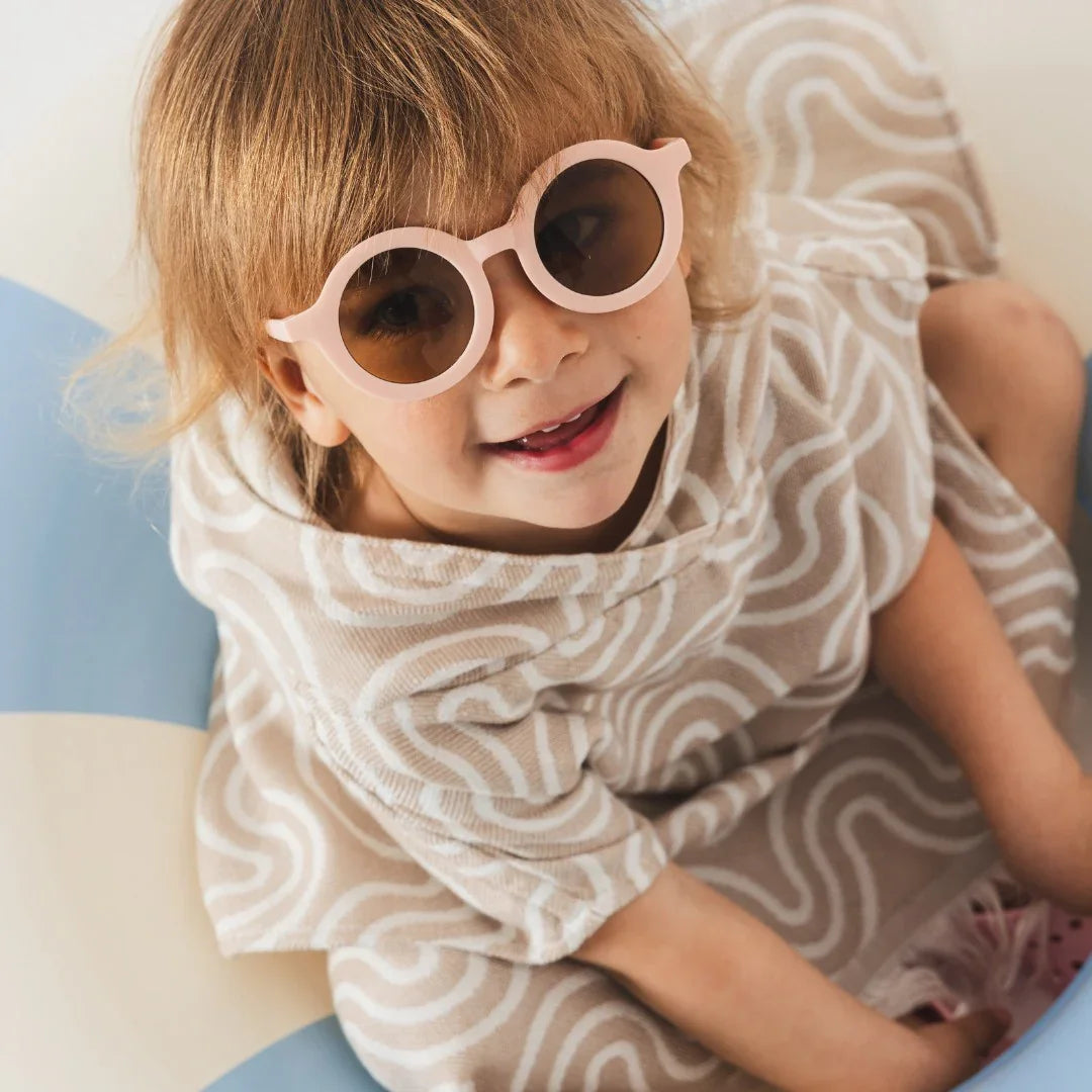 Child wearing sand-colored bamboo kids bath poncho with white swirl pattern and hood