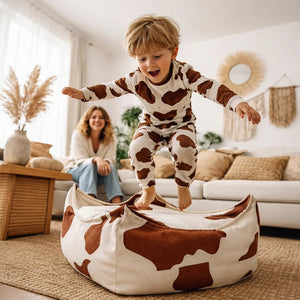 Enfant sautant sur un pouf carré à motif vache dans un salon douillet à la déco naturelle
