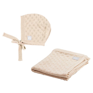 Beige knitted baby bonnet and blanket set with delicate eyelet pattern, folded and side by side