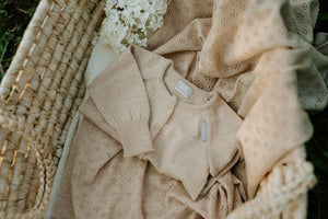Beigefarbene Strickjacke und Decke mit Lochmuster in einem Weidenkorb