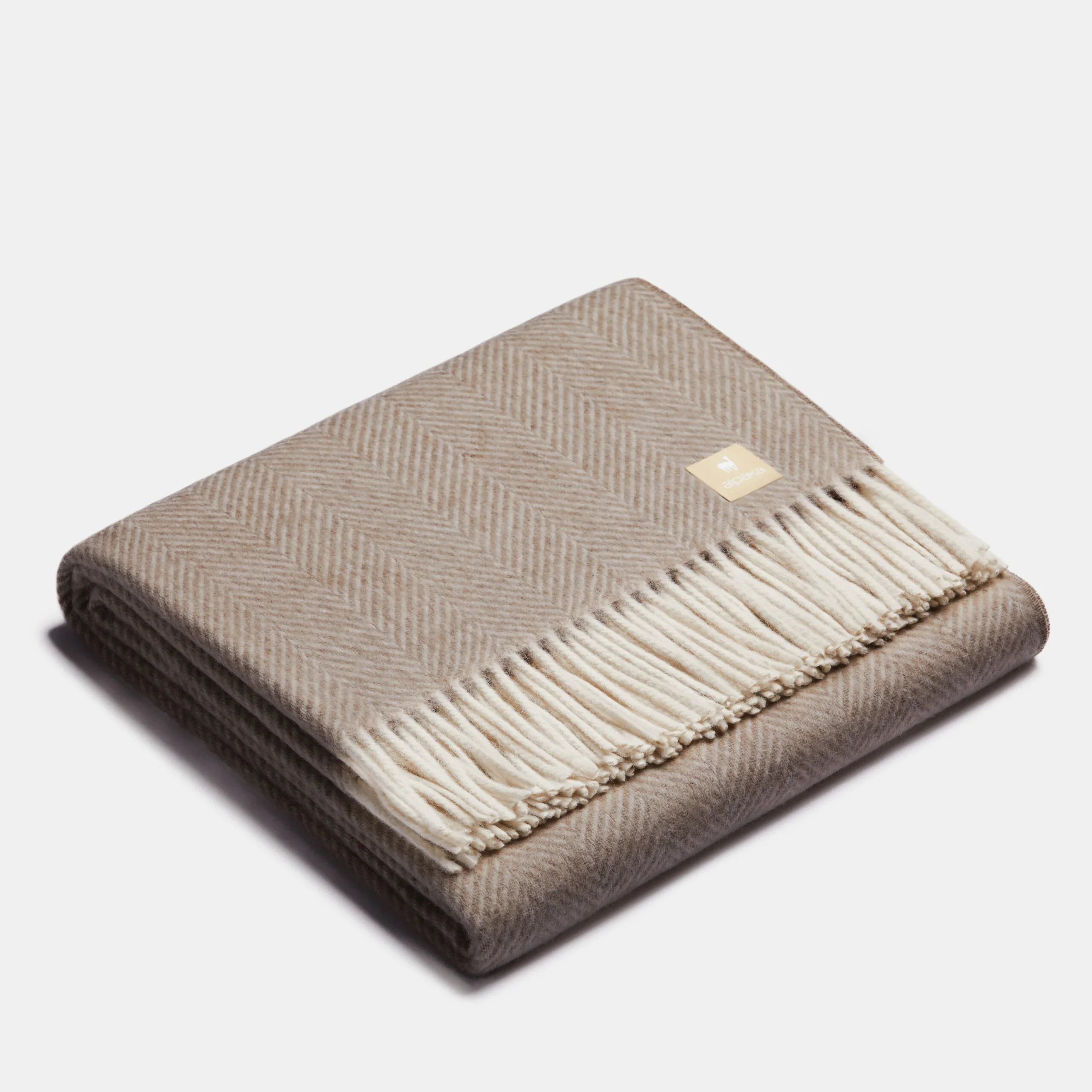 Jeté en laine d'alpaga beige et blanc à motif chevrons, plié, avec franges blanches et étiquette de marque ALPAKA
