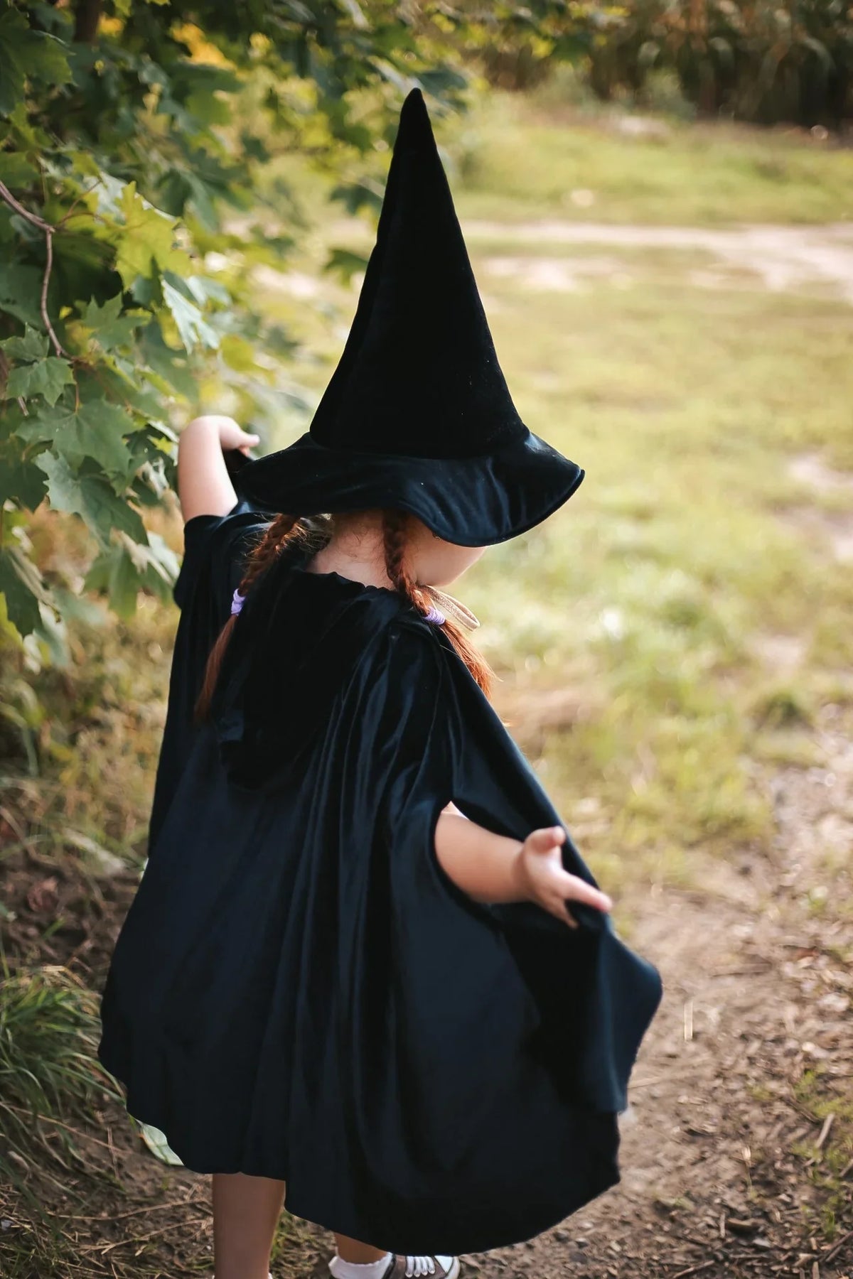 Back view of child wearing flowing black Moi Mili cape and pointed hat outdoors