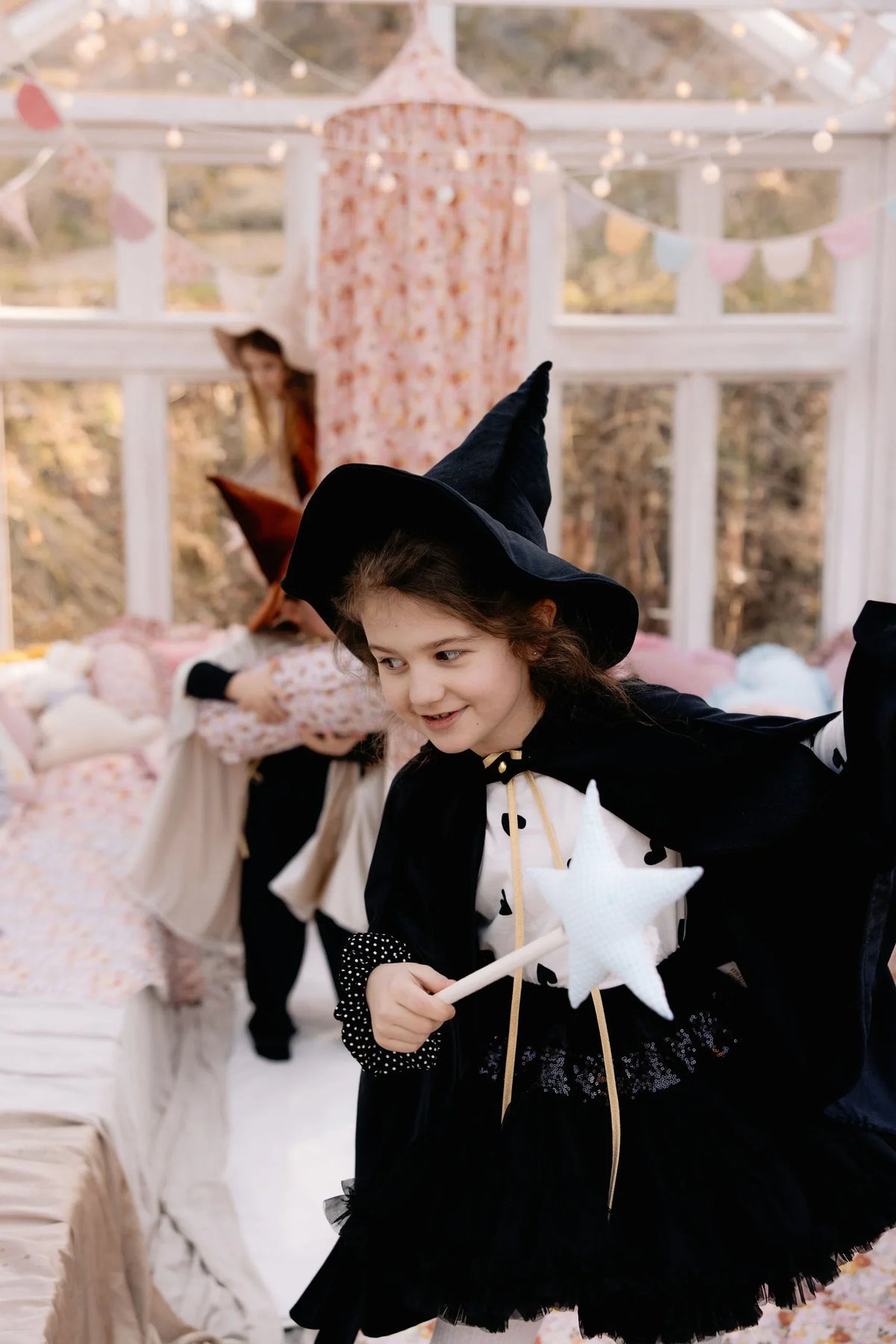 Child wearing flowing black Moi Mili cape and pointed hat while holding a white star wand