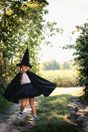 Child spinning in flowing black magic cape on an outdoor path
