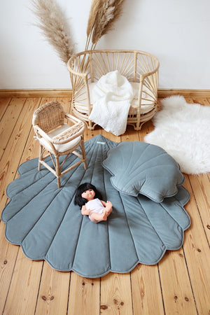 Blue shell playmat styled in a natural rattan nursery with a doll, matching cushion and wooden flooring
