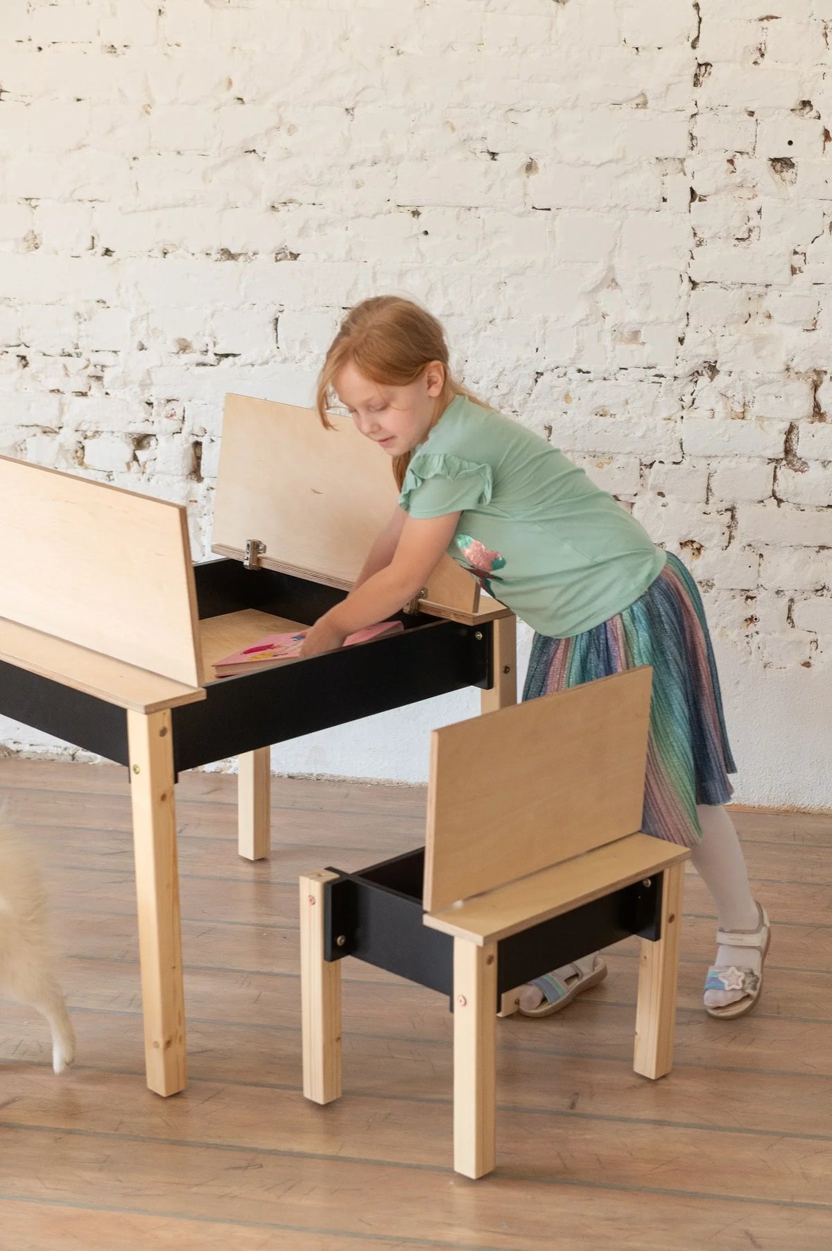 Child organising supplies inside black Smart Storage Table with chair storage open