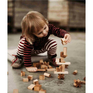 Enfant créant une structure équilibrée avec des blocs en bois naturel, favorisant l'apprentissage Montessori, la motricité fine et le jeu imaginatif sans écran.