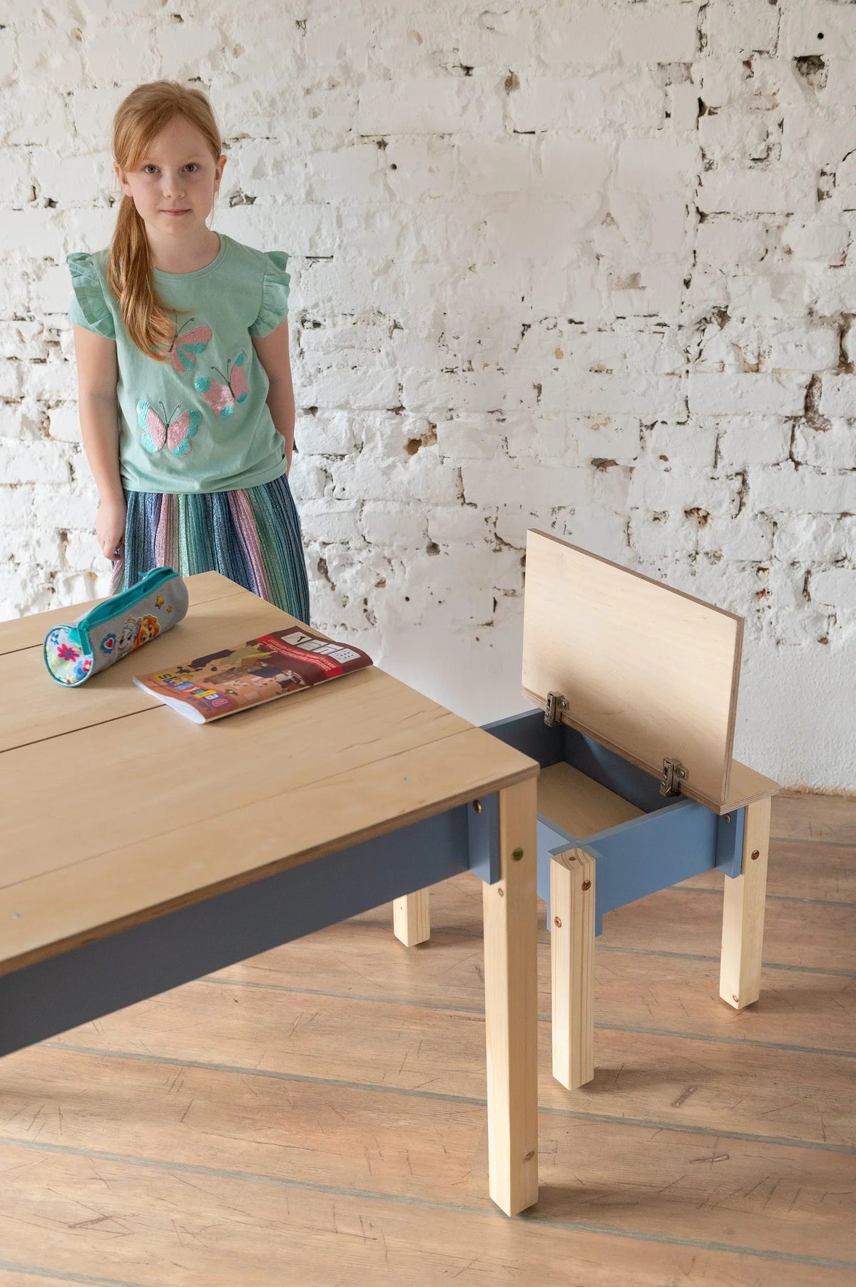 Child standing beside Dusty Blue Smart Storage Table with chair storage compartment open