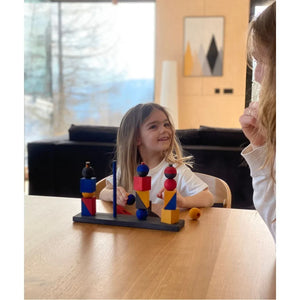 Enfant jouant avec un jeu d'empilement en bois coloré à table, favorisant l'apprentissage Montessori, la coordination, la créativité et le jeu sans écran.